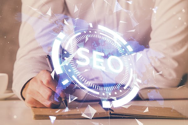 Person writing in a notebook with a digital overlay of the word "SEO," symbolizing digital marketing strategies and services.