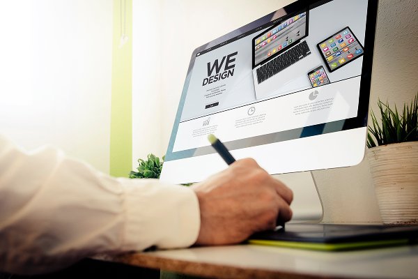 Person using a stylus on a tablet while viewing a computer screen displaying website design elements, emphasizing digital marketing services.